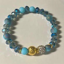 Load image into Gallery viewer, Blue Skies II - Light blue iridescent ceramic beads with dark teal blue crystals, gold disc spacers, and white crystal pavé bead
